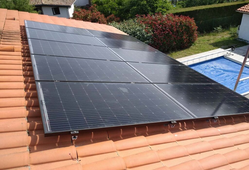 Panneaux solaires sur un toit en tuiles, avec une piscine en arrière-plan dans un jardin verdoyant dans les Landes.