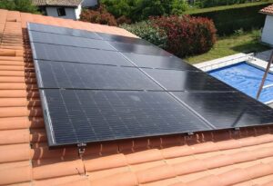 Panneaux solaires sur un toit en tuiles, avec une piscine en arrière-plan dans un jardin verdoyant dans les Landes.