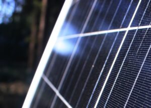 Panneau solaire éclairé par le soleil, entouré d'ombres d'arbres en arrière-plan flou.