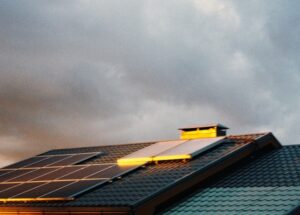 Panneaux solaires sur un toit incliné, illuminés par la lumière du soleil couchant, ciel nuageux en arrière-plan.