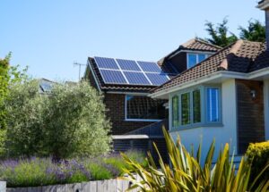 Maison avec panneaux solaires sur le toit, entourée de végétation, ciel bleu en arrière-plan.