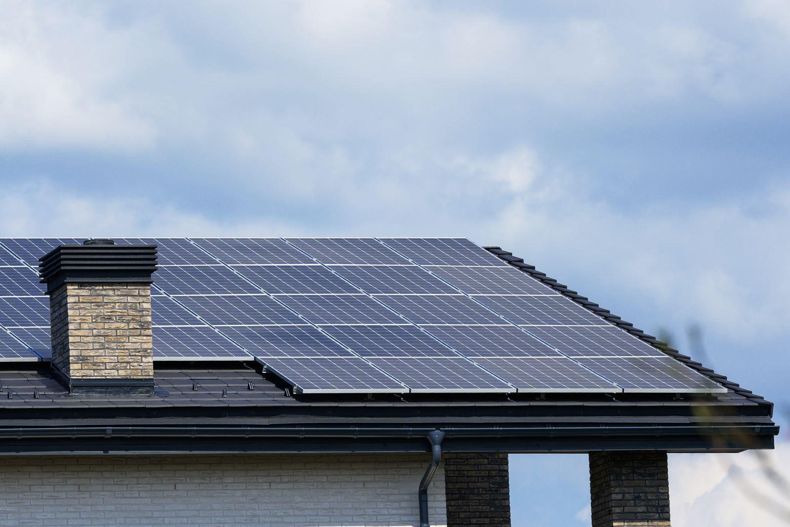 Toiture de maison équipée de panneaux solaires sous un ciel nuageux